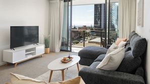 Un salón moderno con un televisor de pantalla plana, un sofá gris y un balcón con vistas a la ciudad.