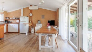 Una cocina con una mesa de madera, sillas blancas, un refrigerador y un televisor.