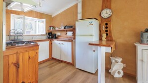Una cocina compacta con armarios de madera, un refrigerador blanco, un reloj y una ventana.