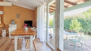 Un comedor con una mesa y sillas de madera, un televisor y vistas al jardín a través de amplios ventanales.