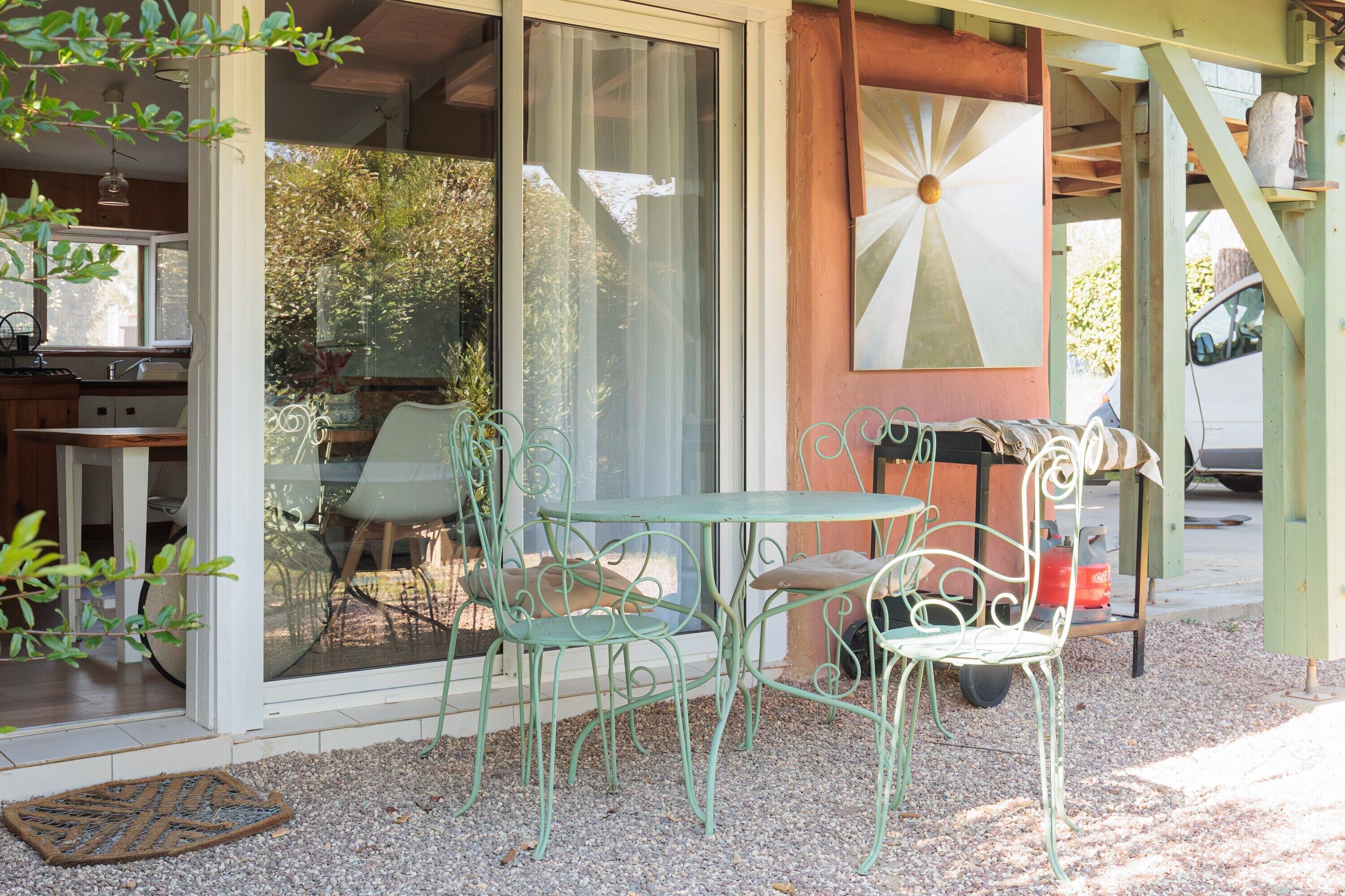 A patio with metal chairs and a table, a sliding glass door, and a view of the garden.
