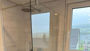 A modern bathroom with a glass-enclosed shower, a toilet, and a window offering a city view.