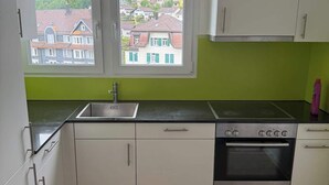A kitchen with white cabinets, a Bosch oven, a sink, and a window with a view of houses.