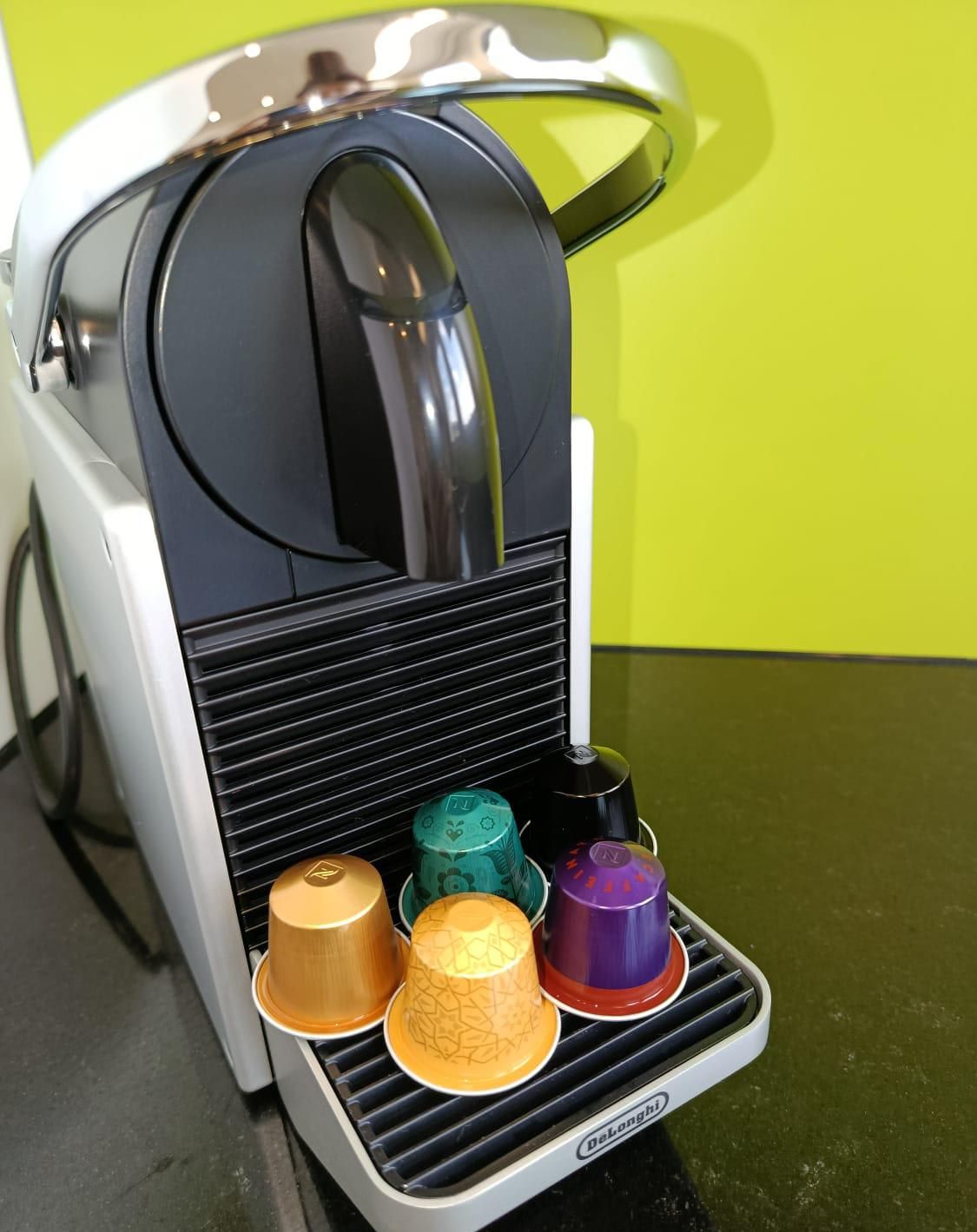 Una cafetera con cuatro cápsulas de café de colores sobre la bandeja de goteo.
