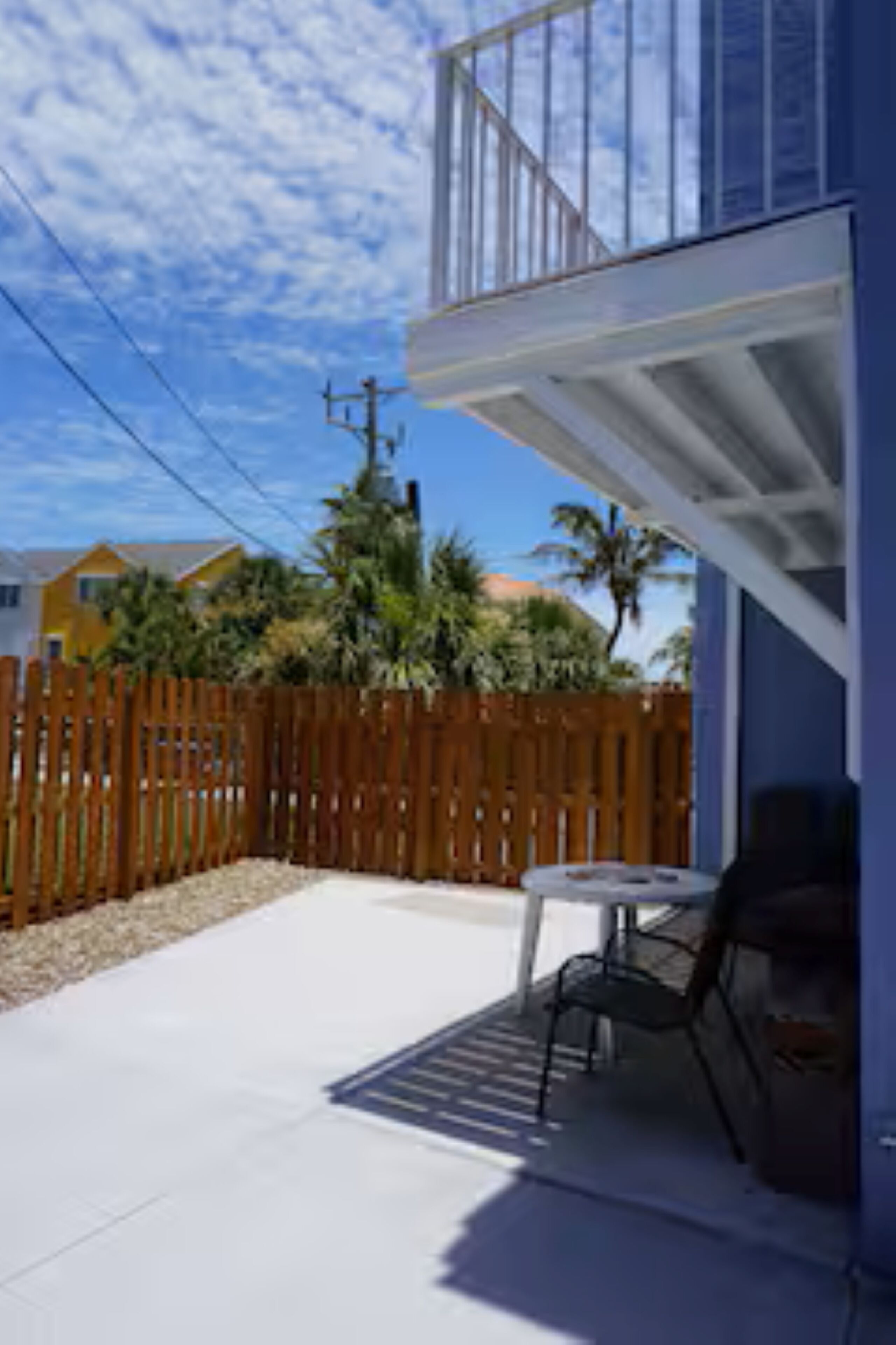 A covered patio with a table and chairs, a wooden fence, and houses in the background.
