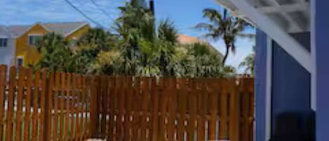 A covered patio with a table and chairs, a wooden fence, and houses in the background.