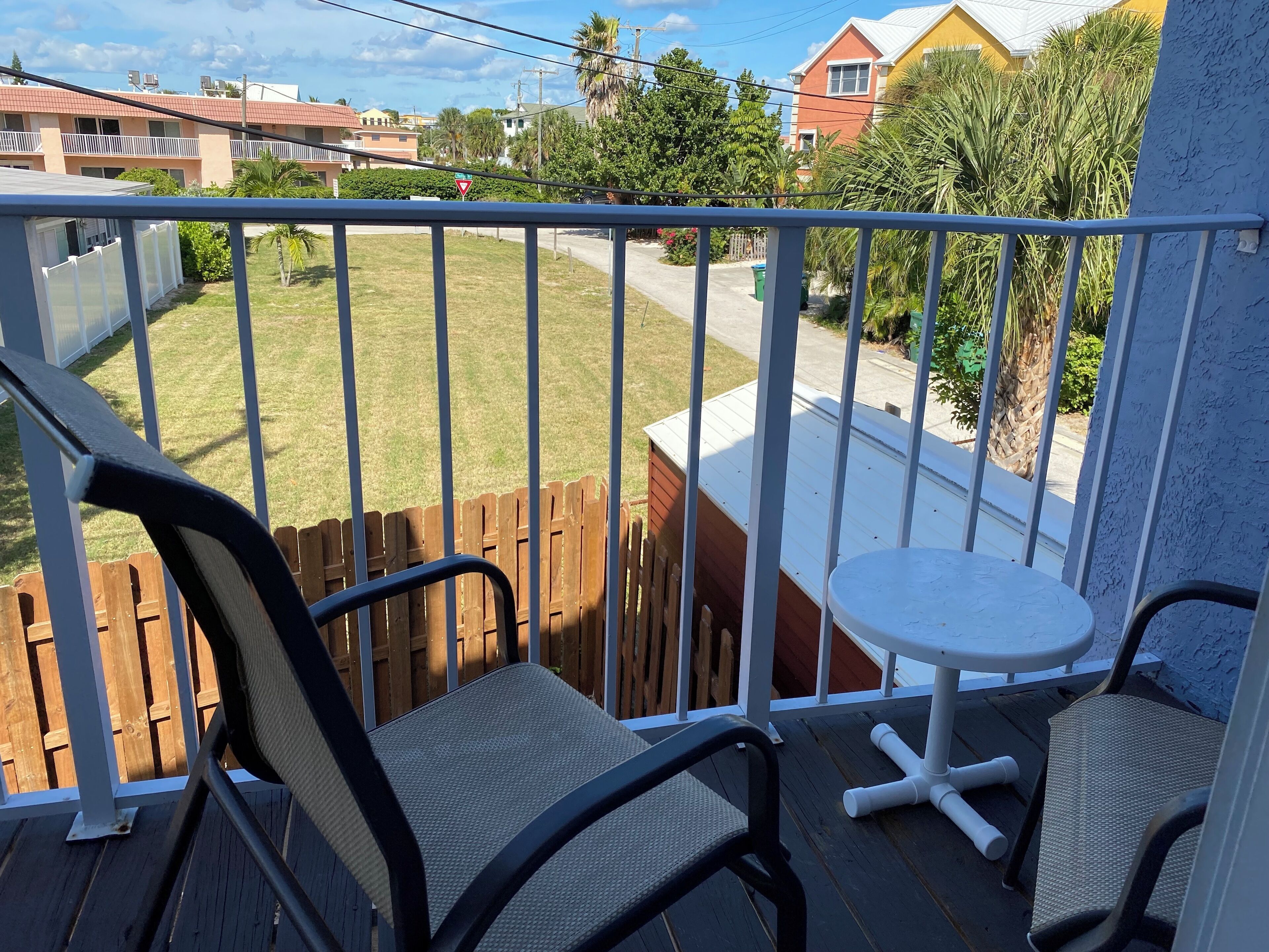 A balcony with a view of a residential street, a wooden fence, and a small white table.