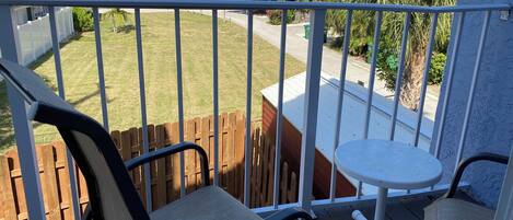 A balcony with a view of a residential street, a wooden fence, and a small white table.