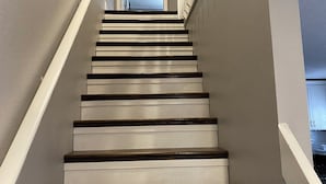 Eine Treppe mit weißen Stufen und dunklen Holztritten, die zu einer Tür oben führt.