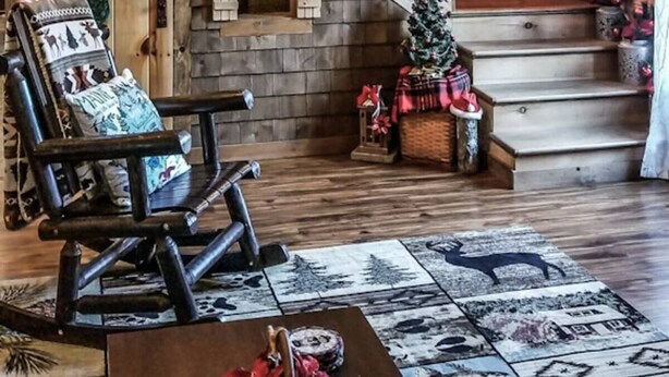 Ein Holzblockhaus-Interieur mit einer weihnachtlich geschmückten Treppe, einem Schaukelstuhl und einem Kamin.