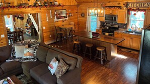 Ein gemütliches Blockhaus-Interieur mit Holzvertäfelung, einer Essecke, einer Küche und einem Wohnzimmer mit Couch und Kamin.
