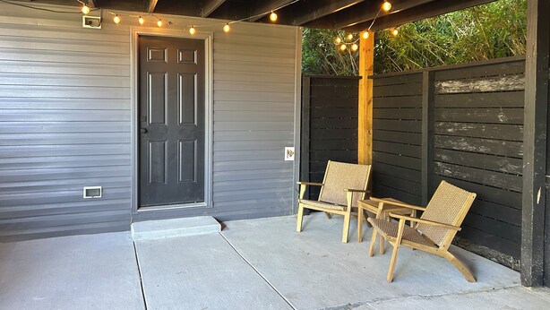 A covered patio with a door, two wicker chairs, and string lights. - Cozy Tiny House in Scottsburg (Scottsburg)