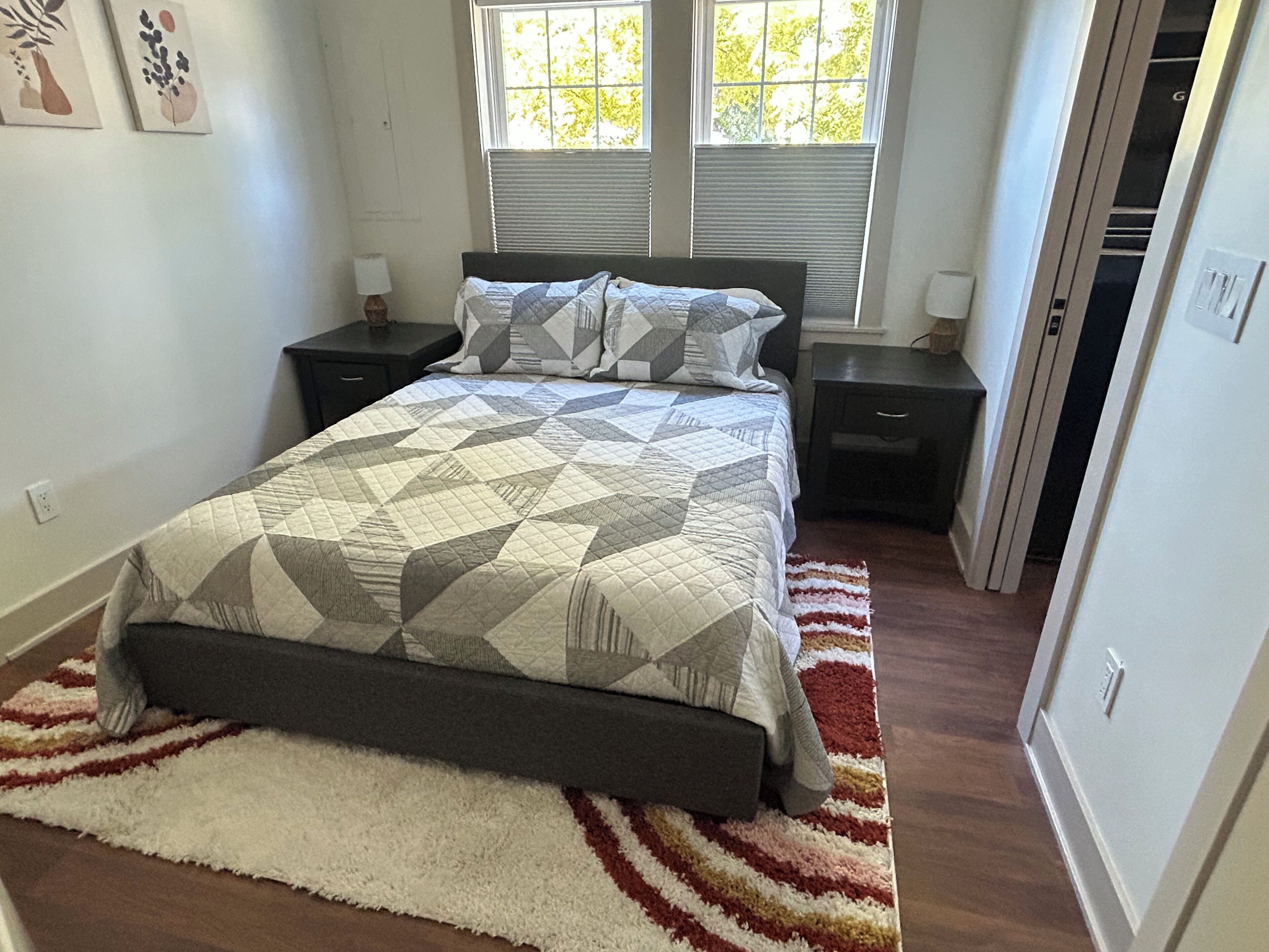 A bedroom with a bed, two nightstands, a window with blinds, and a door.