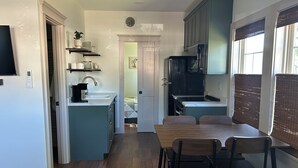 A compact kitchen with a dining area, wooden flooring, and a view of the adjacent bedroom. - Cozy Tiny House in Scottsburg (Scottsburg)