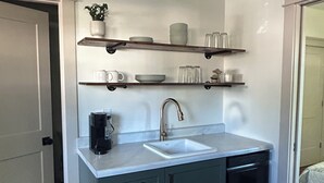A compact kitchen with a sink, cabinets, and shelves above the countertop. - Cozy Tiny House in Scottsburg (Scottsburg)