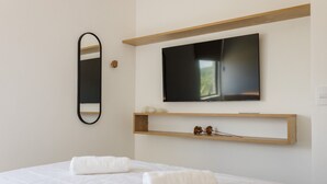 A modern bedroom with a bed, a TV mounted on the wall, and a wooden shelf below. - TMH - Essence Condominium in Porto de Pedras/al (Porto de Pedras)