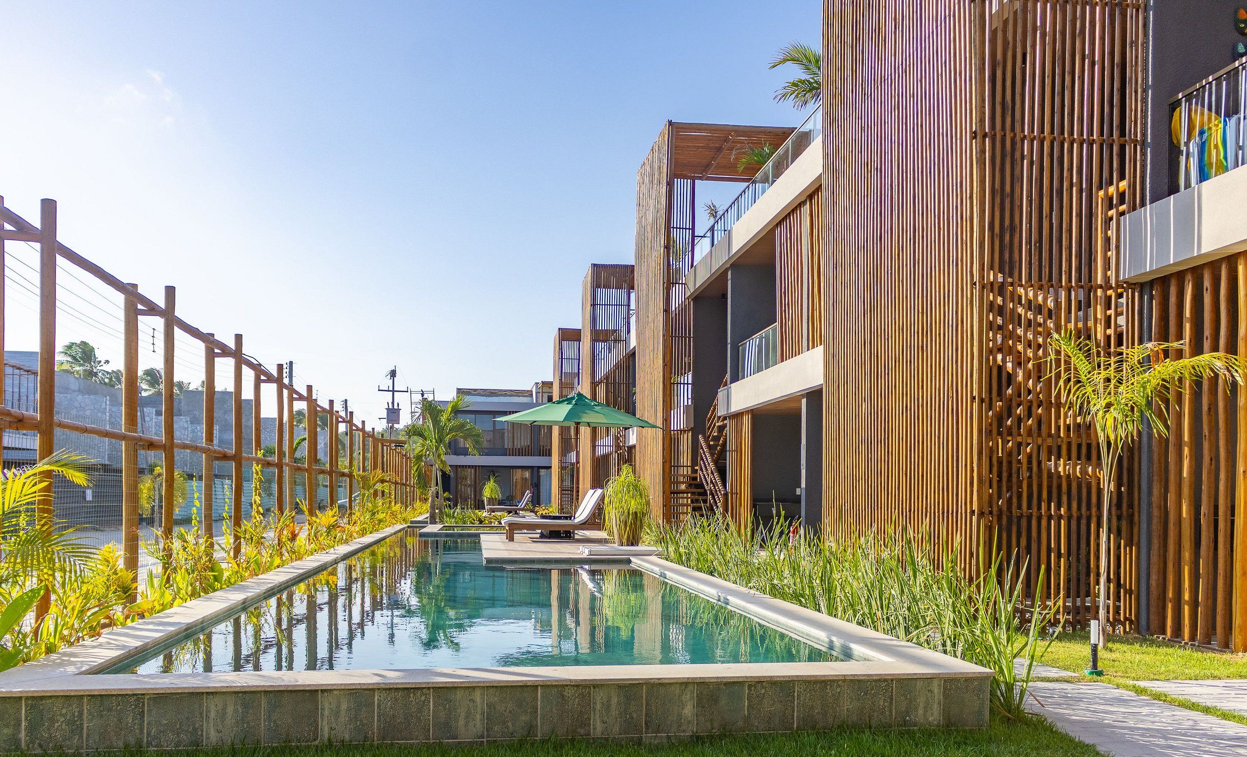 Un área de piscina moderna con una piscina cristalina, sillas de descanso y una valla de bambú.