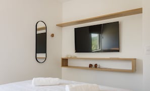Ein modernes Schlafzimmer mit einem Bett, einem an der Wand montierten Fernseher und einem Holzregal darunter.