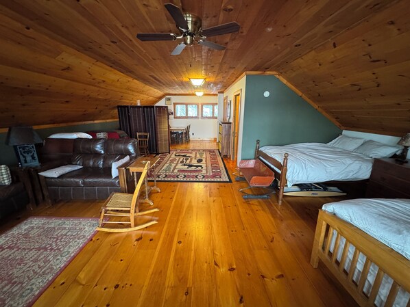Un dormitorio acogedor en el ático con pisos de madera, un ventilador de techo, una cama, un sillón mecedora y una mesita.