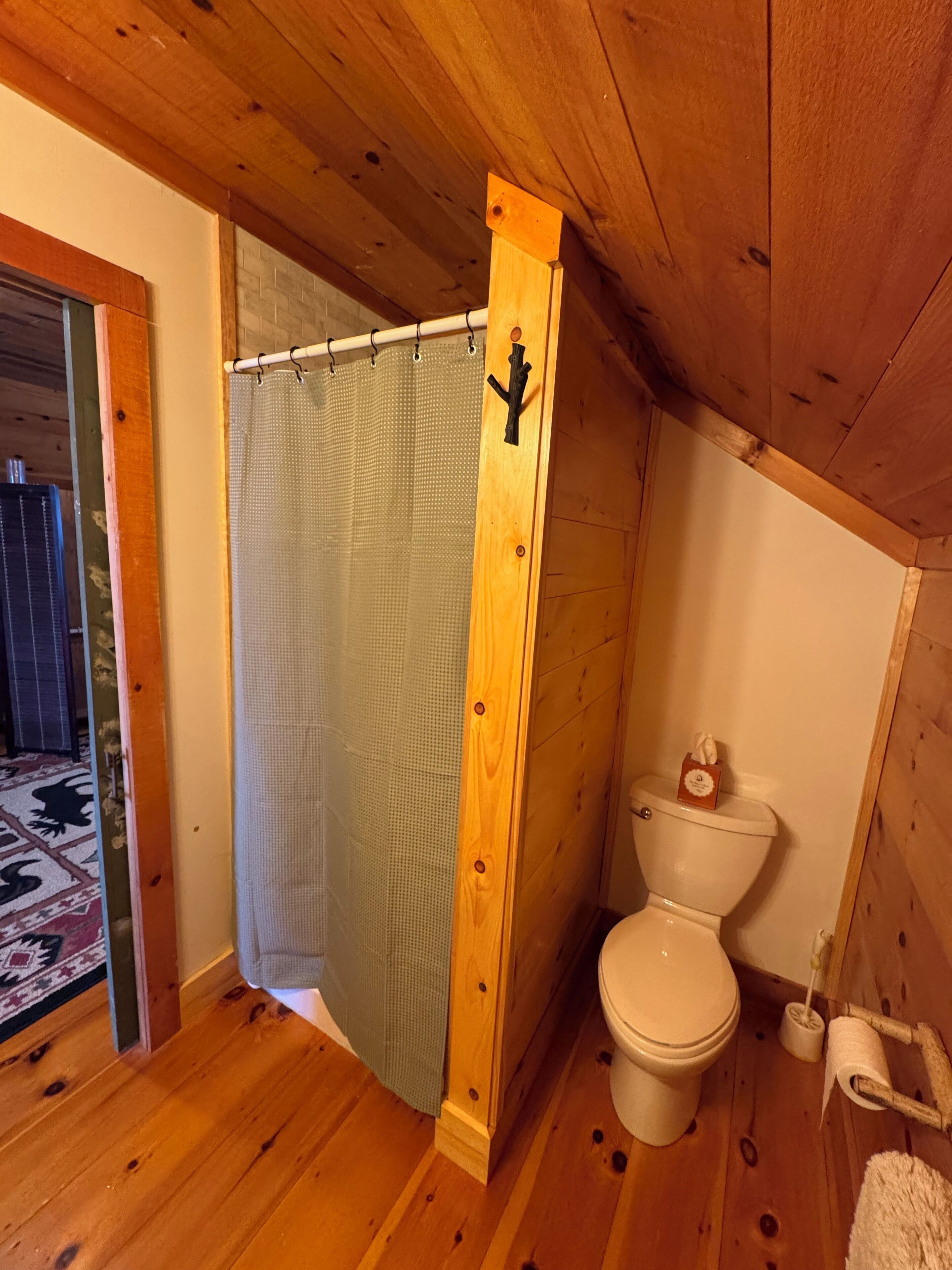 A wooden-paneled bathroom with a shower curtain, toilet, and a towel rack.
