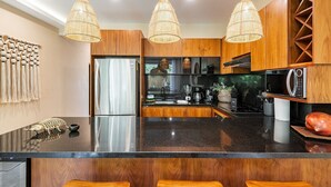 A modern kitchen with wooden cabinets, a black granite countertop, and three hanging wicker chandeliers. - •| Condo Boutique Swim Up in Tulum P/6 • Naaj Tun• (Tulum)