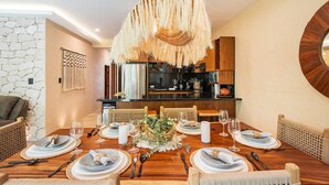 A dining area with a wooden table set for six, surrounded by wicker chairs, a decorative centerpiece, and a modern chandelier. - •| Condo Boutique Swim Up in Tulum P/6 • Naaj Tun• (Tulum)