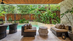 A covered outdoor seating area with wicker furniture, a stone wall, and lush greenery. - •| Condo Boutique Swim Up in Tulum P/6 • Naaj Tun• (Tulum)