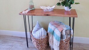 Een houten console tafel met een spiegel, een bloempot en rieten manden met kussens.