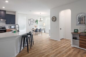 A modern kitchen with dark cabinets, a white island, and bar stools. - Near Tesla w/ EV charging - Extended Stays welcome (Manor)