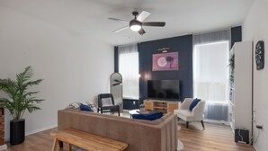 Uma sala de estar com sofá, um banco, televisão e ventilador de teto.
