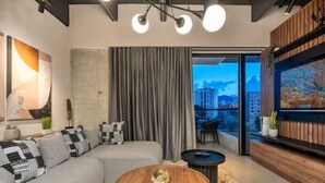 A modern living room with a grey sofa, a round coffee table, and a large window with curtains. - City Lights in El Poblado 2 bedrooms, 2 Bathrooms, 2 Air Conditioners,2 Safes (Medellín)