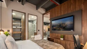 A modern hotel room with a large bed, a TV mounted on the wall, a wooden panel design, and a cityscape view. - City Lights in El Poblado 2 bedrooms, 2 Bathrooms, 2 Air Conditioners,2 Safes (Medellín)