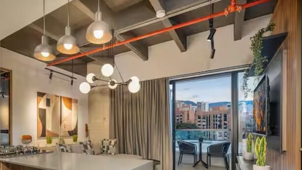A modern kitchen with a central island, bar stools, pendant lighting, and a view of the city through large windows. - City Lights in El Poblado 2 bedrooms, 2 Bathrooms, 2 Air Conditioners,2 Safes (Medellín)