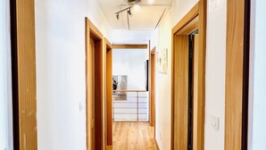 A narrow hallway with wooden doors and a wooden floor leading to a kitchen area.