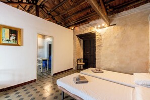 Una habitación con dos camas, techo de madera, una puerta que da a otra habitación y un cuadro en la pared.