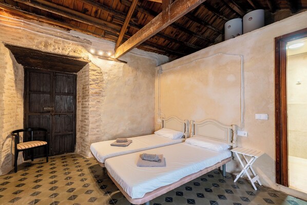 Habitación con dos camas, un banco, una puerta y piso de baldosas.