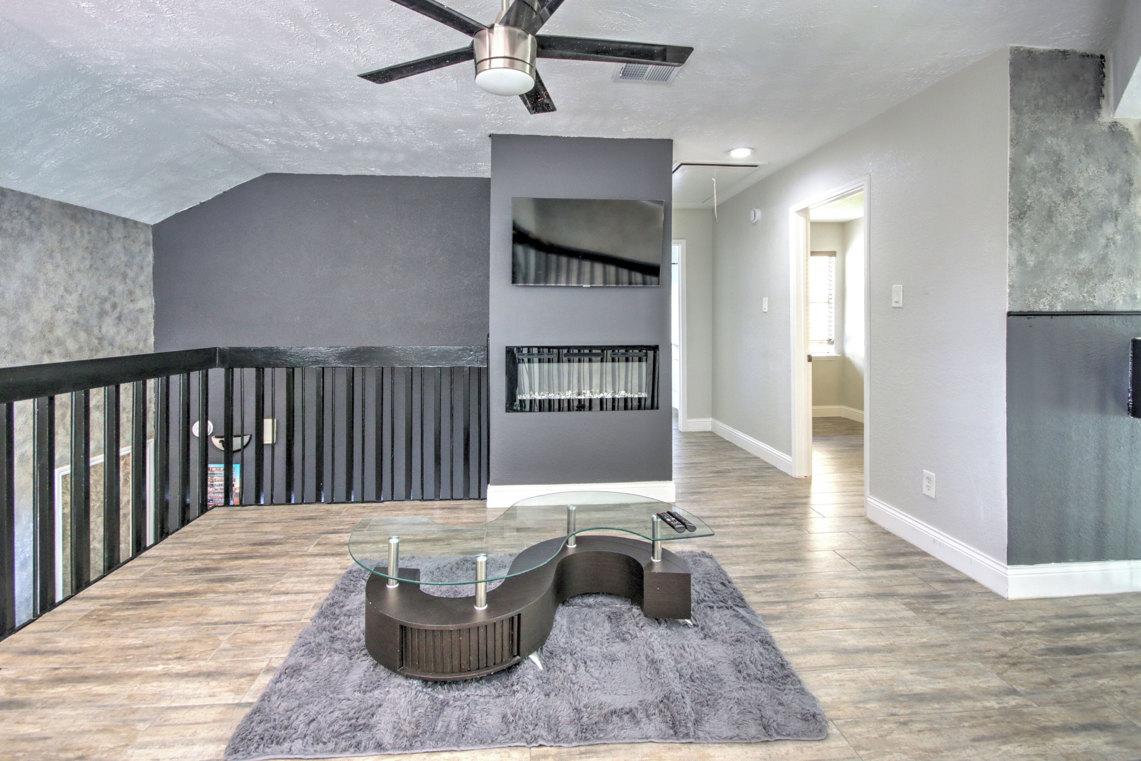 A modern interior with a curved glass coffee table, a ceiling fan, and a staircase leading to another level.