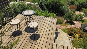Une terrasse en bois avec une table et des chaises, entourée d’une végétation luxuriante et offrant une vue sur des collines lointaines.