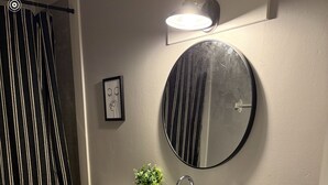 Et badeværelse med et hvidt underskab, bordplade i sort og et rundt spejl.