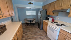 A kitchen with wooden cabinets, a white stove, a microwave, and a dining table with chairs. - MinCo Properties WV, Carswell Hollow Overlook  (Kimball)