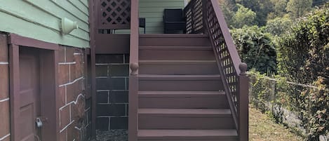 Eine hölzerne Treppe führt zu einer überdachten Veranda mit Blick auf einen bewaldeten Hang.