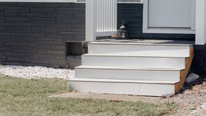 A house with a white front door, a small porch with steps, and a window with a grid pattern.