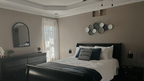 A modern bedroom with a black bed, a dresser, a mirror, and decorative wall art.