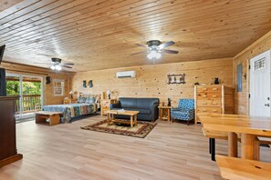 Un salon spacieux avec un plafond en bois, un canapé en cuir noir, une table basse en bois et une table à manger avec des bancs.
