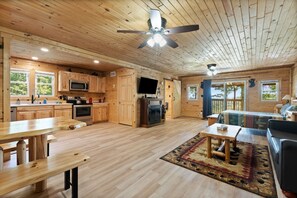 A spacious living area with wooden floors, a large sofa, a dining table, and a fireplace.