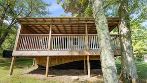 Une terrasse en bois, dotée d’une rambarde et soutenue par des arbres, située dans un environnement naturel.