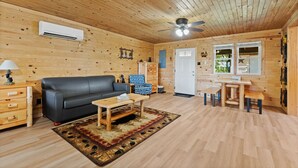 L'intérieur d'un chalet en bois, avec un canapé noir, une table basse en bois et un coin repas comprenant une table et des bancs.