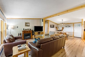 Amplia sala de estar con chimenea, sofás de cuero, televisor y un comedor con muebles de madera.