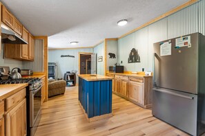 A modern kitchen with wooden cabinets, a stainless steel refrigerator, and a blue island counter.