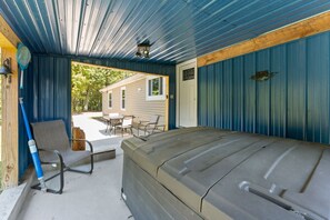Un espacio al aire libre techado con jacuzzi, asientos y vistas a una casa.